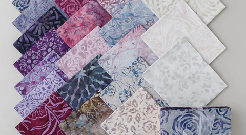 A selection of fat quarter fabrics with floral and nature-inspired batik prints in blue and purple tones from the Tonga Batiks Plumberry collection.
